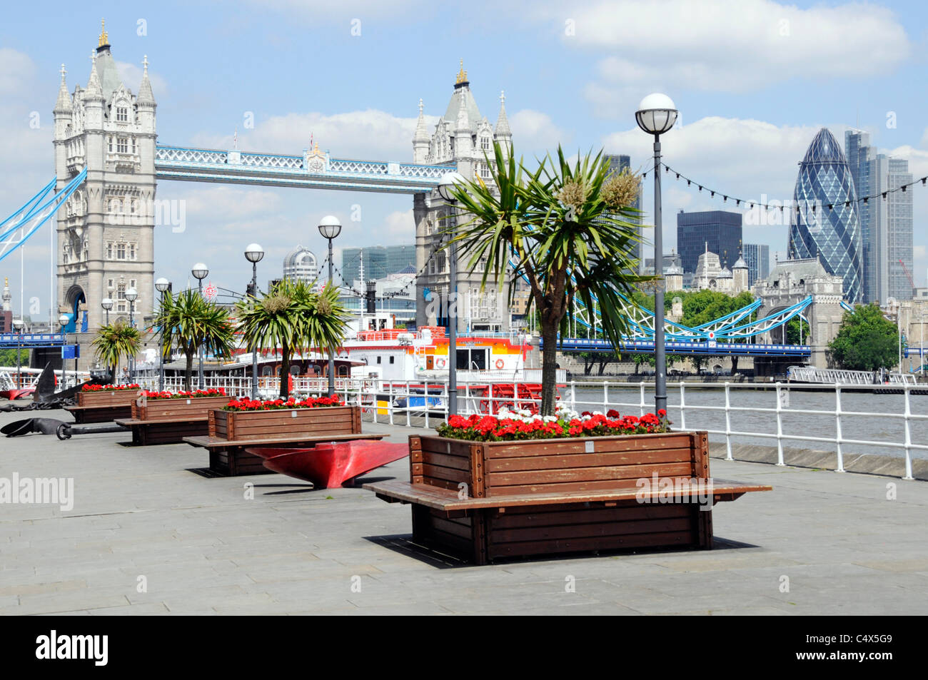 Thames Path Butlers Wharf on River Thames views of Tower Bridge & London skyline Gherkin skyscraper red flower & cordyline trees in planters London UK Stock Photo
