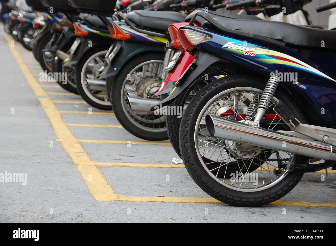 A row of cheap scooters / motorcycles parked in a carpark in Malaysia. Composition focuses on receding row of back wheels. Stock Photo