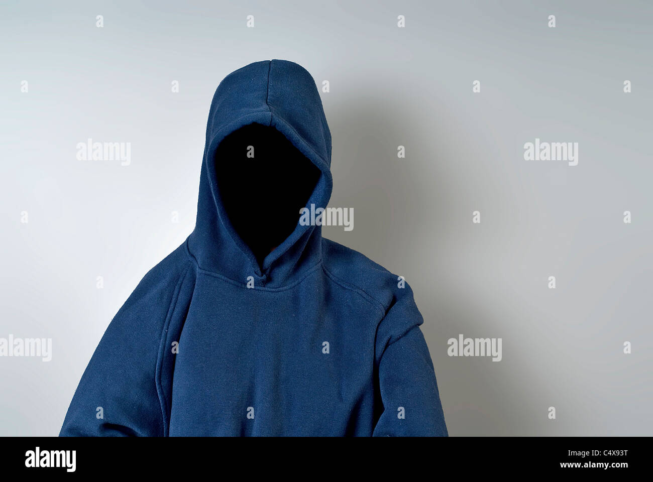A blue hoody with nothing but a dark shadow in place of a face against a white wall with copy-space. Stock Photo