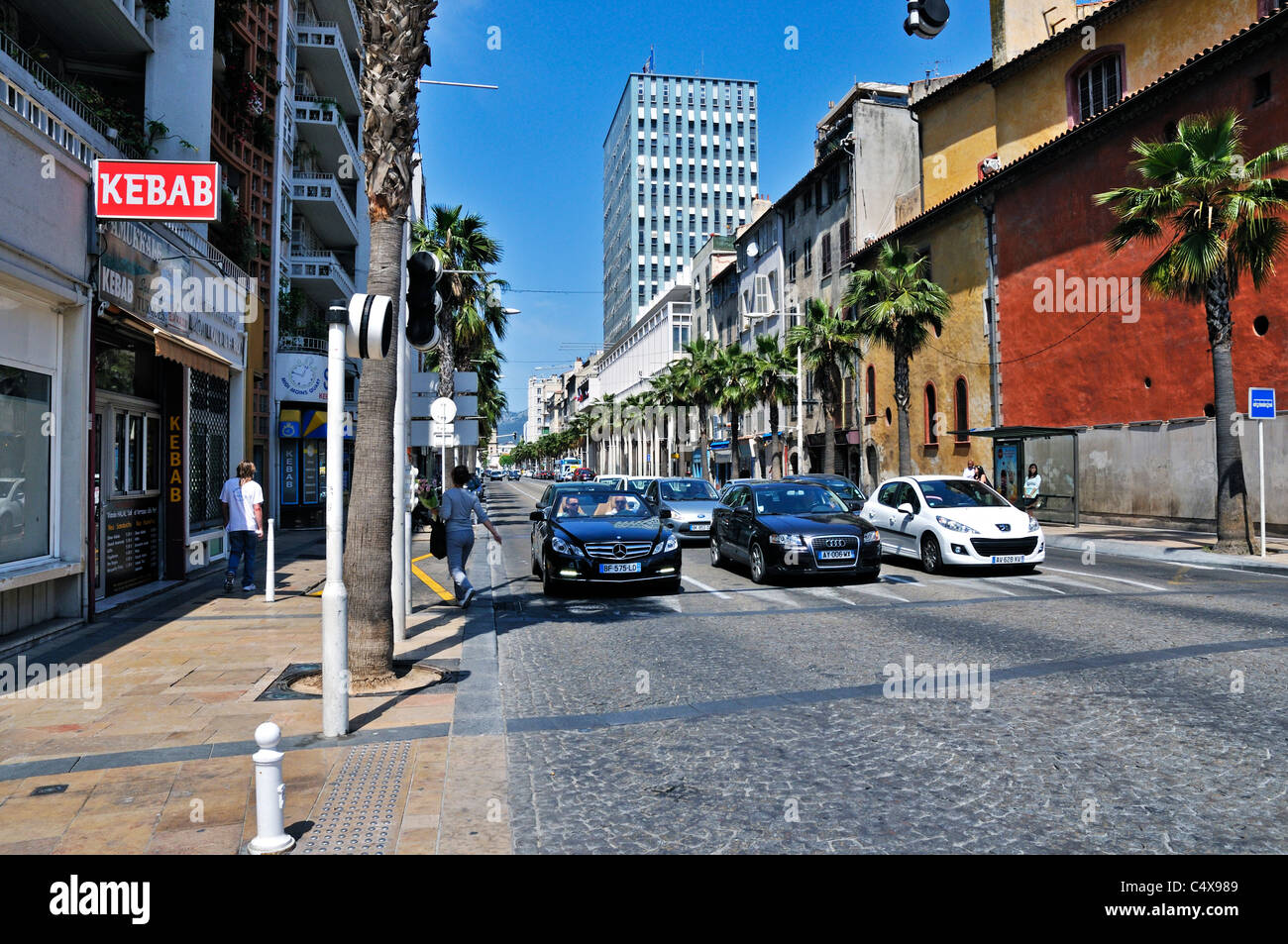 Traffic halted at a pedestrian crossing in a pleasant sunny tree lined avenue with plenty of different shops, Toulon Stock Photo