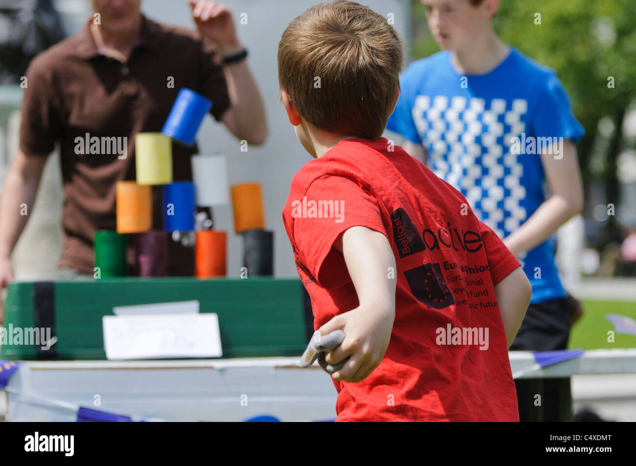 Boy throws bean bag at tins, knocking them over, in fairground game 'Tin Can Alley' Stock Photo