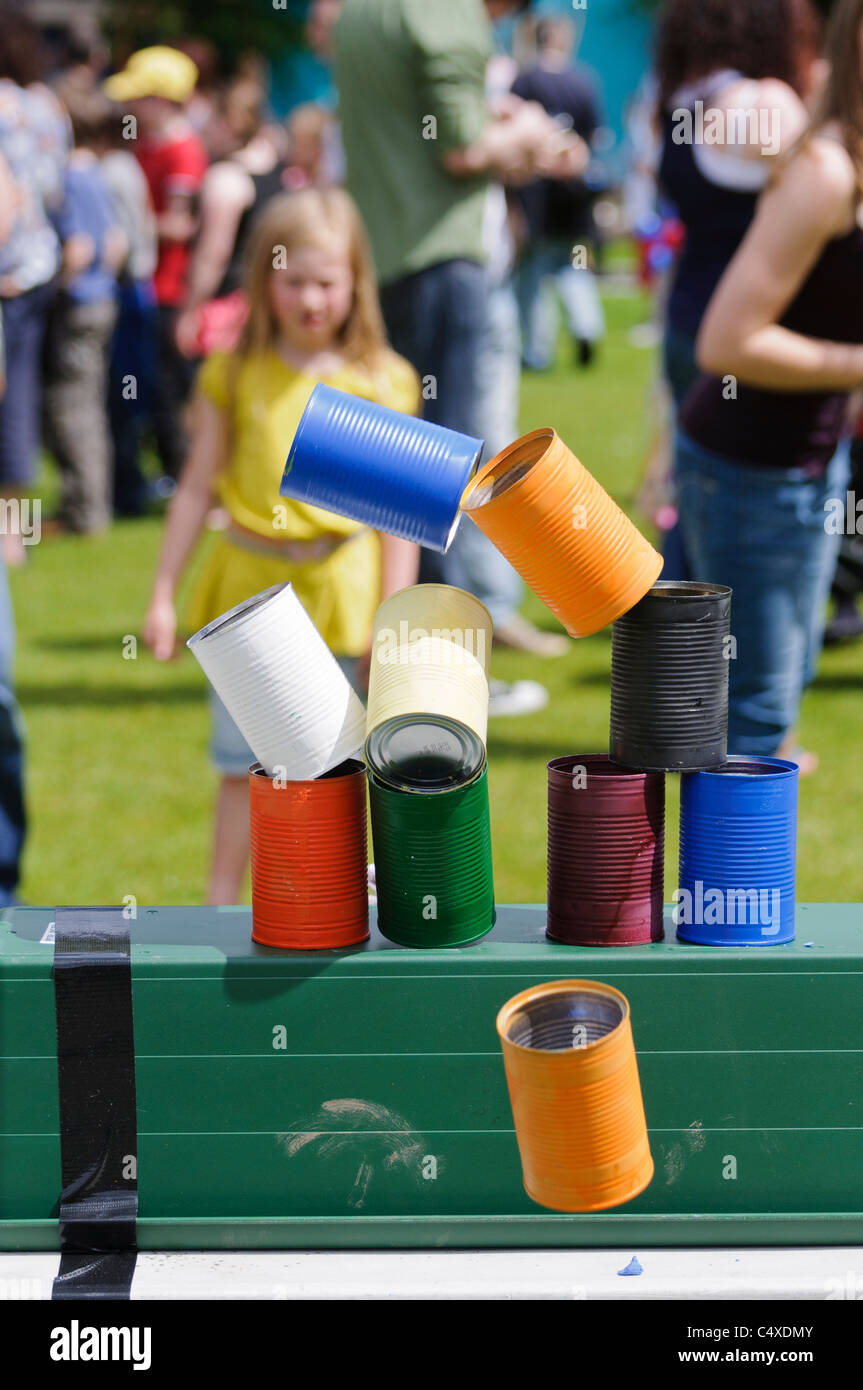 Girl throws bean bag at tins, knocking them over, in fairground game 'Tin Can Alley' Stock Photo