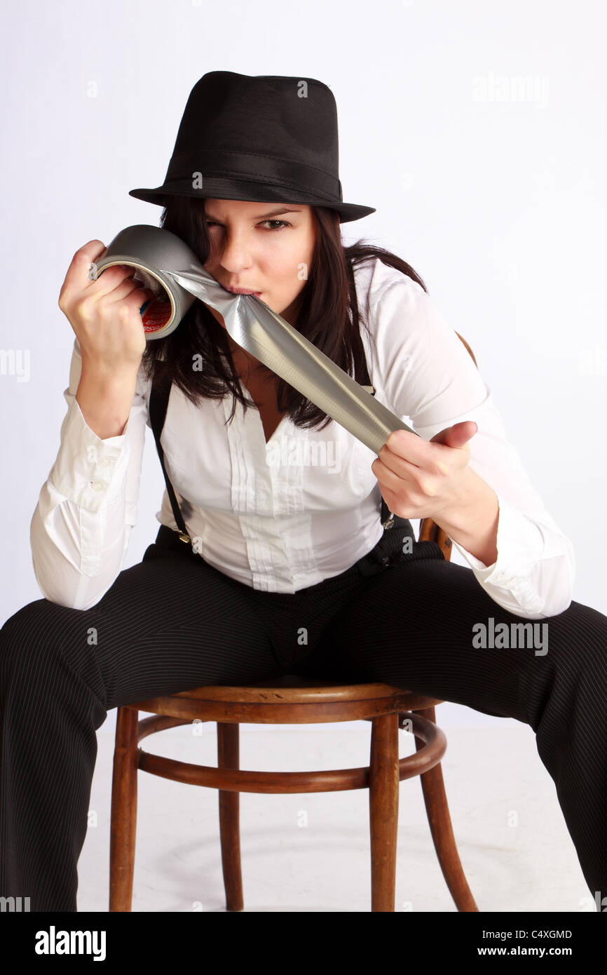 Young beautiful brunette woman in hat with brim bytes a gray tape with her teeth Stock Photo