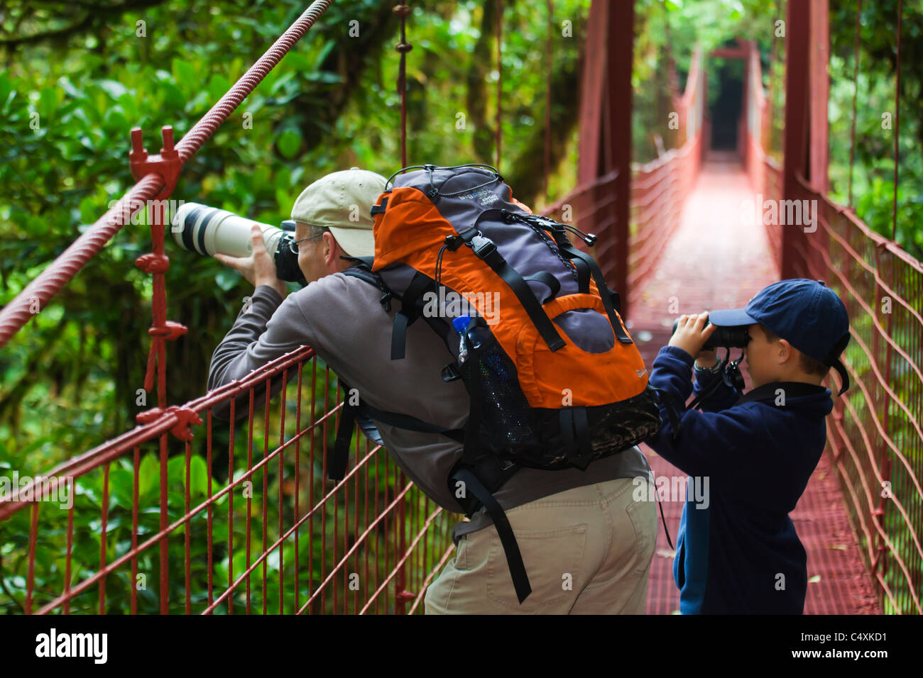 Ecotourists father and son with camera backpack and binoculars on hanging bridge canopy walkway in Monteverde Cloudforest Stock Photo