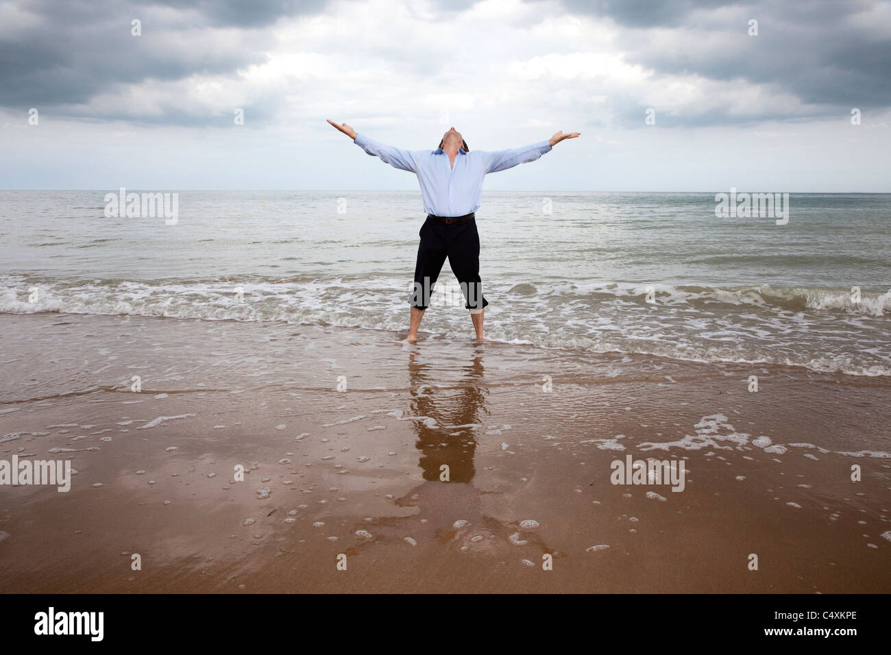 Fully clothed man standing in the sea with arms out looking to the sky. Stock Photo