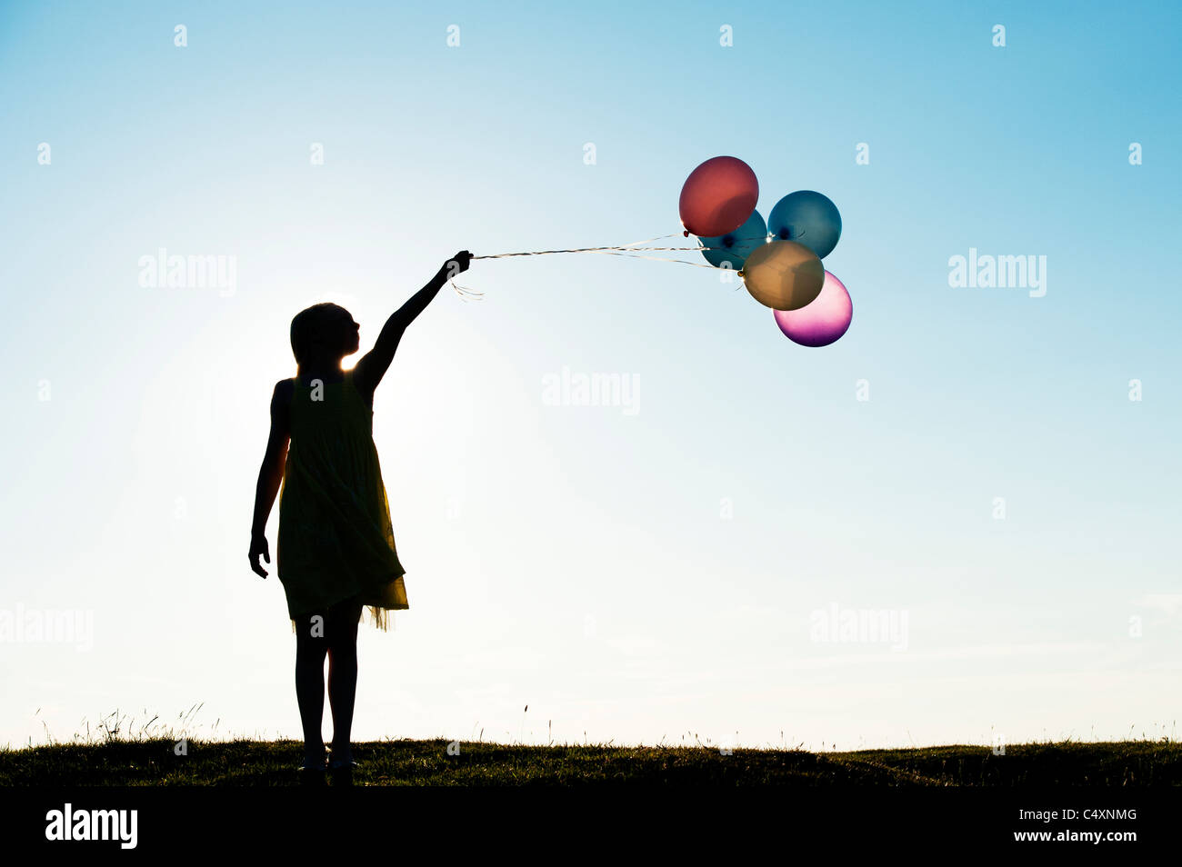 Silhouette of a young girl holding coloured balloons at sunset Stock