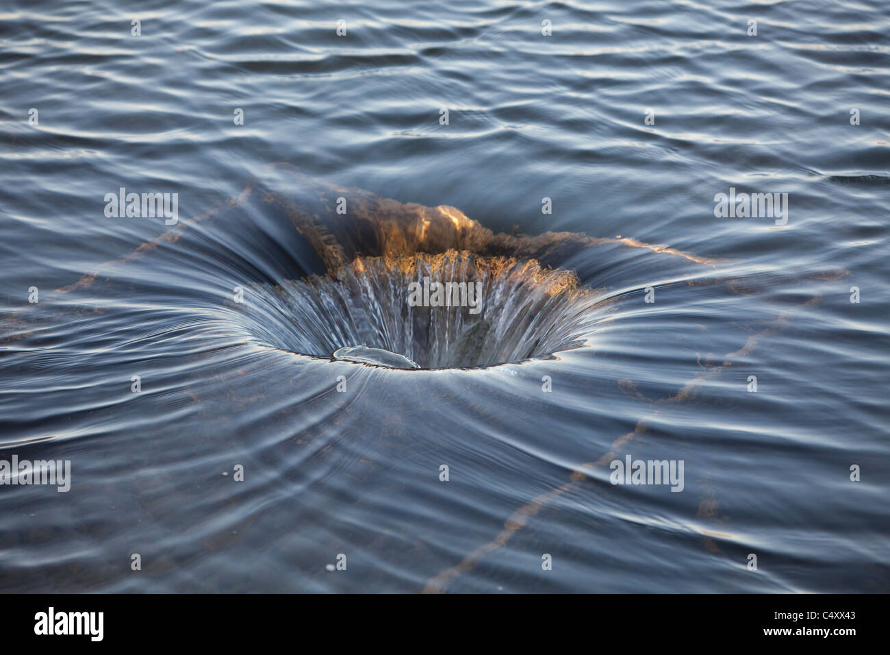 Water in one of a chain of small spring-fed lakes pours down outlet pipe that leads into lower lake on a ranch in west Texas USA Stock Photo