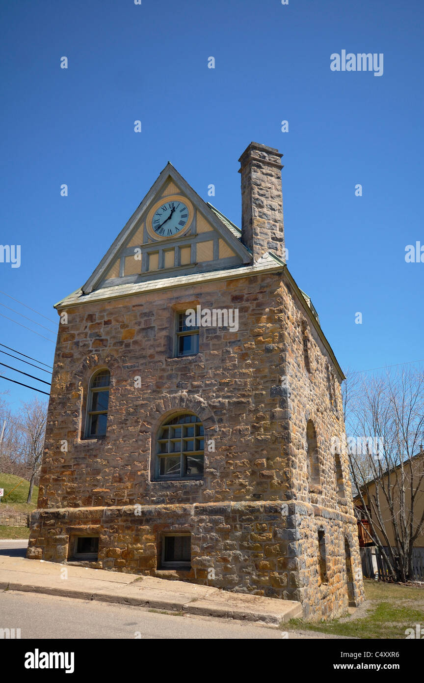 A old stone building with a clock in the roof's peak. Chimney on side of building and building rests on a hillside. Stock Photo
