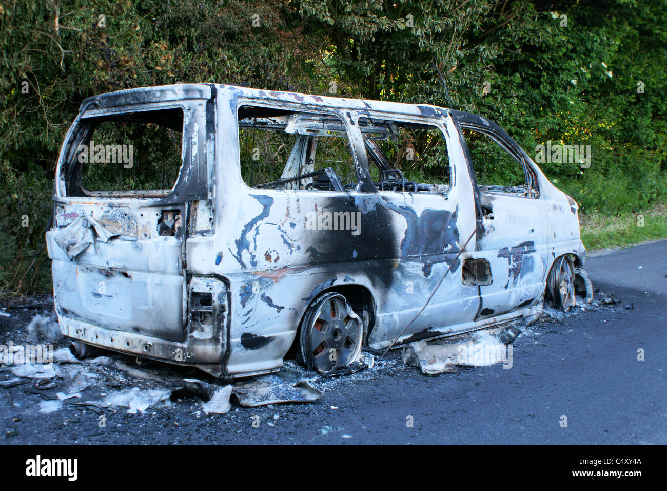 Vandalised burnt out van abandoned on the road. Stock Photo