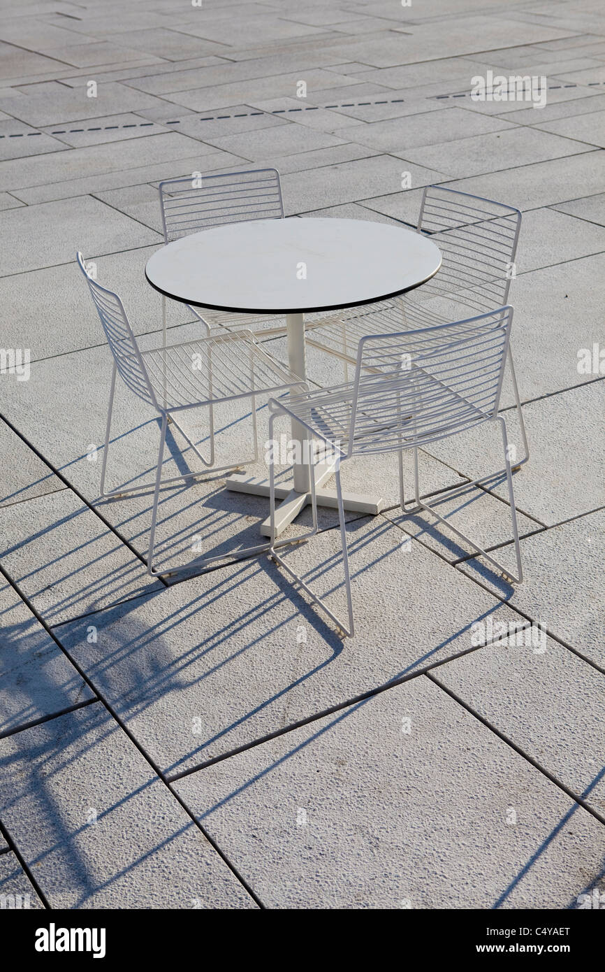 Rounded table/s and chairs on a tiled floor shadow is revealed through a descending sunset Stock Photo