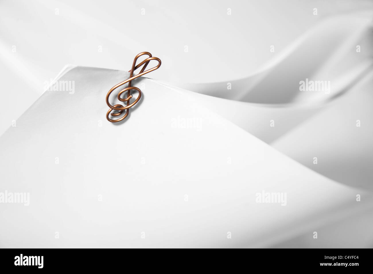Paper clip shaped like a music clef clipped to white paper. Stock Photo