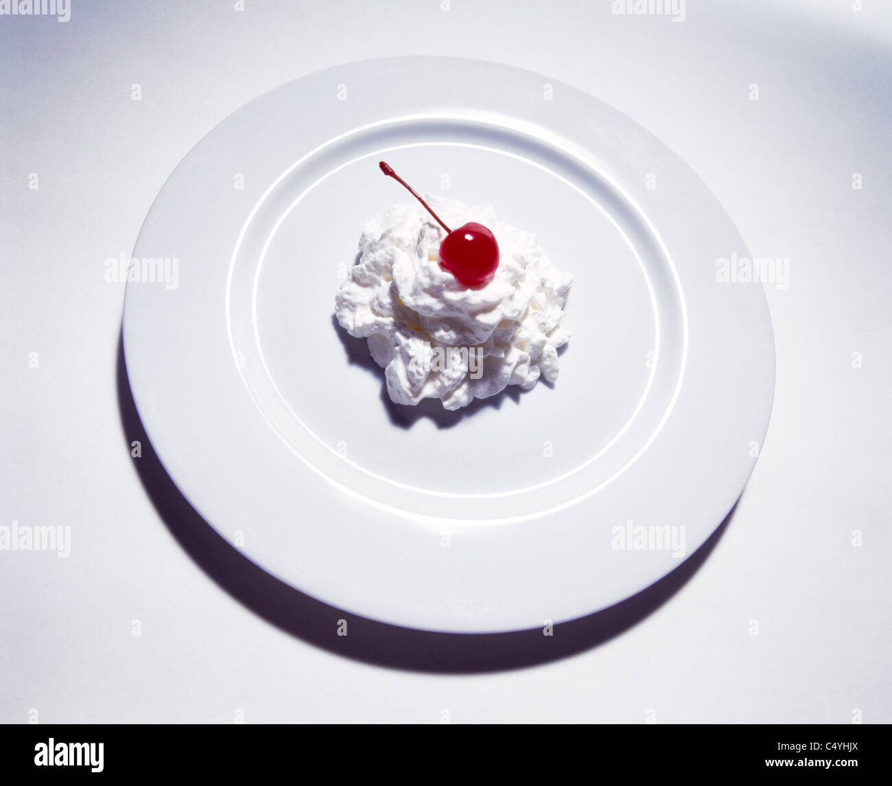 A white plate with whipped cream and red stemmed cherry Stock Photo