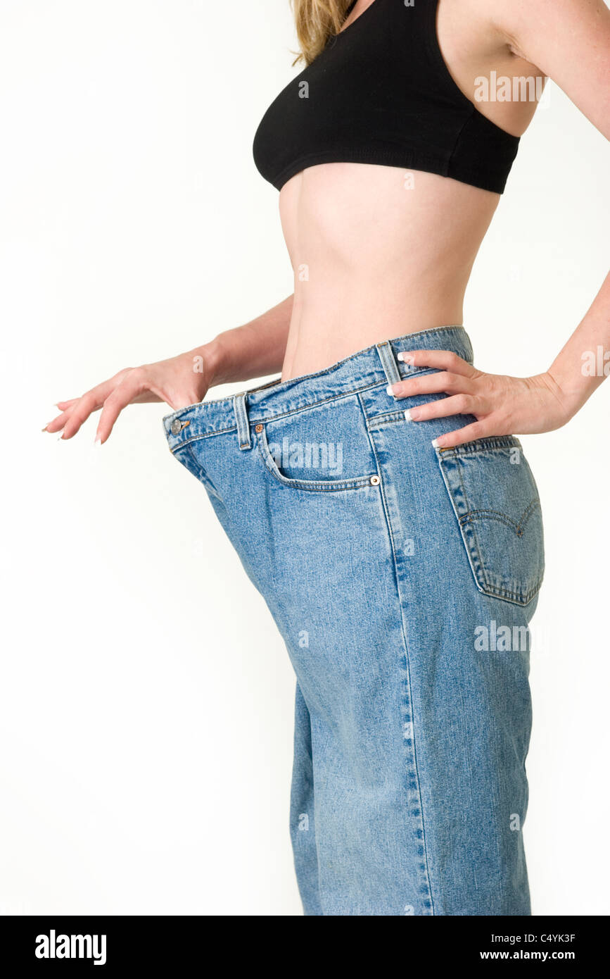 Woman demonstrating weight loss by wearing an old pair of jeans and holding  out to show how big the pants are Stock Photo - Alamy