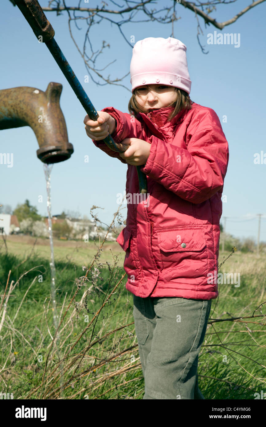 little girl and the old pump in field Stock Photo