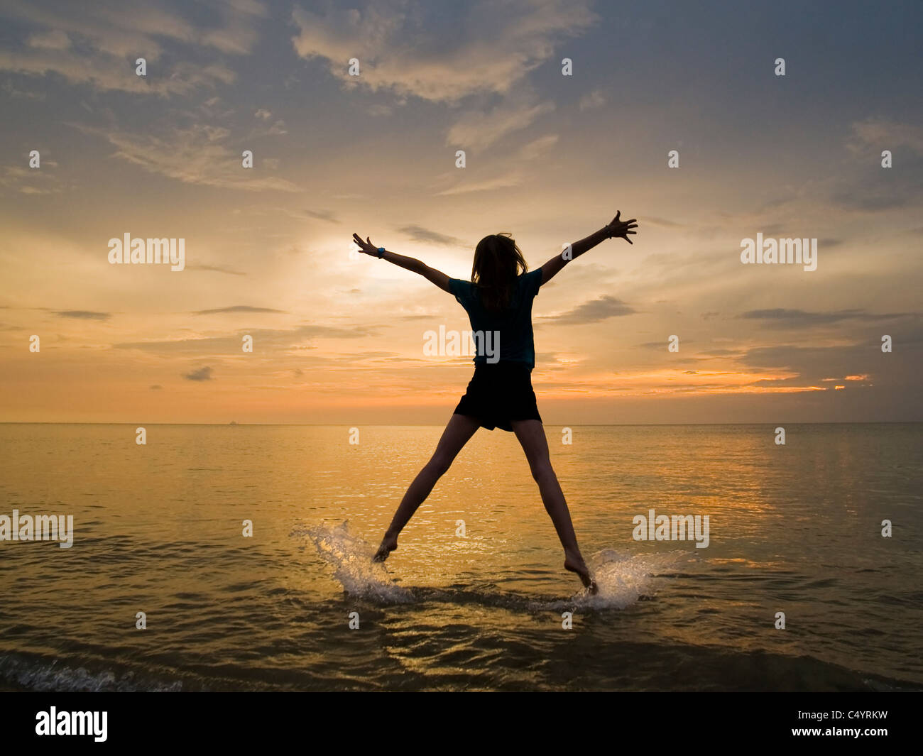 A young woman doing a star jump, jumping for joy and enjoying her freedom on the beach at sunset. Stock Photo