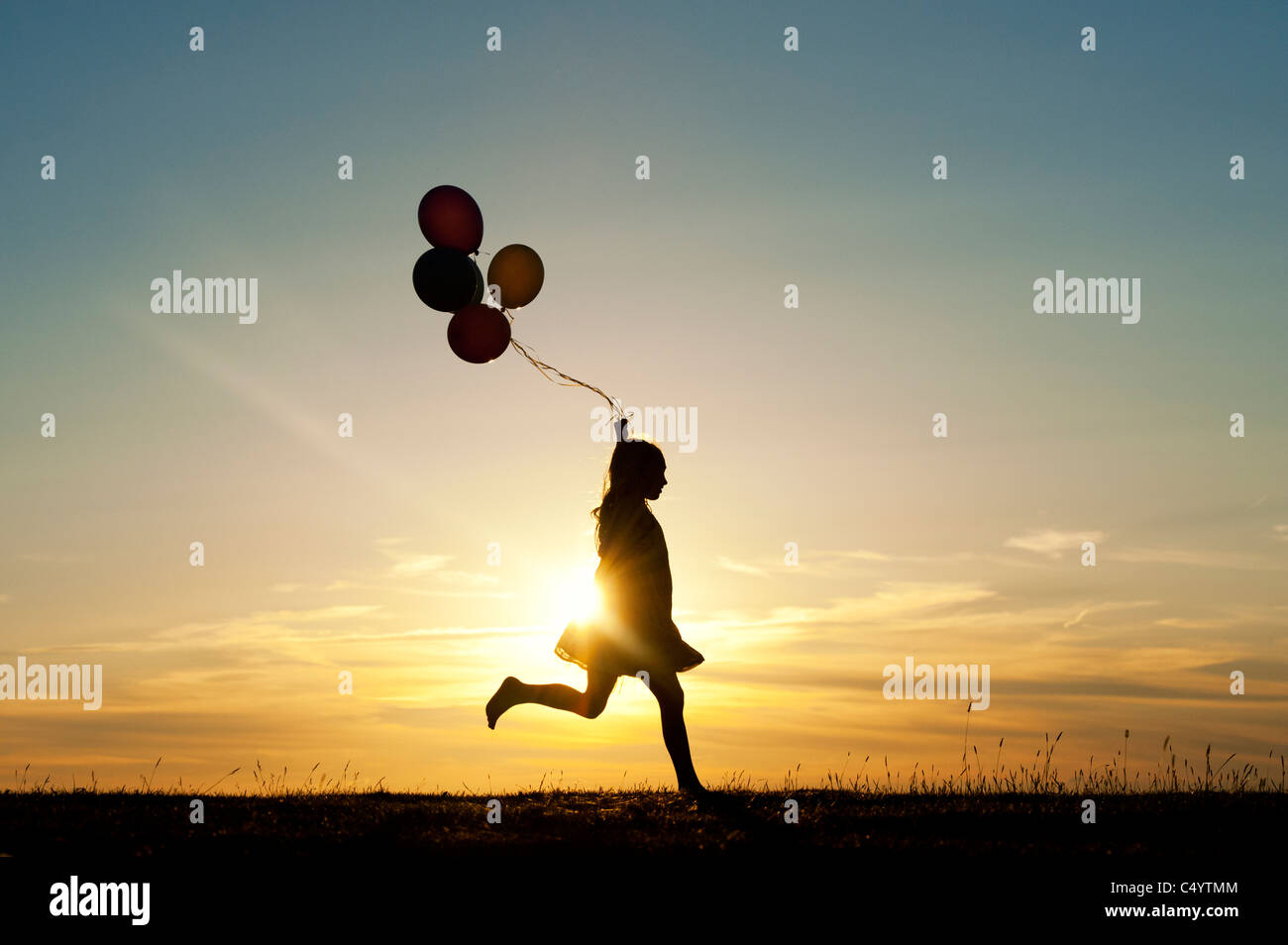 Silhouette of a young girl running with balloons at sunset Stock Photo