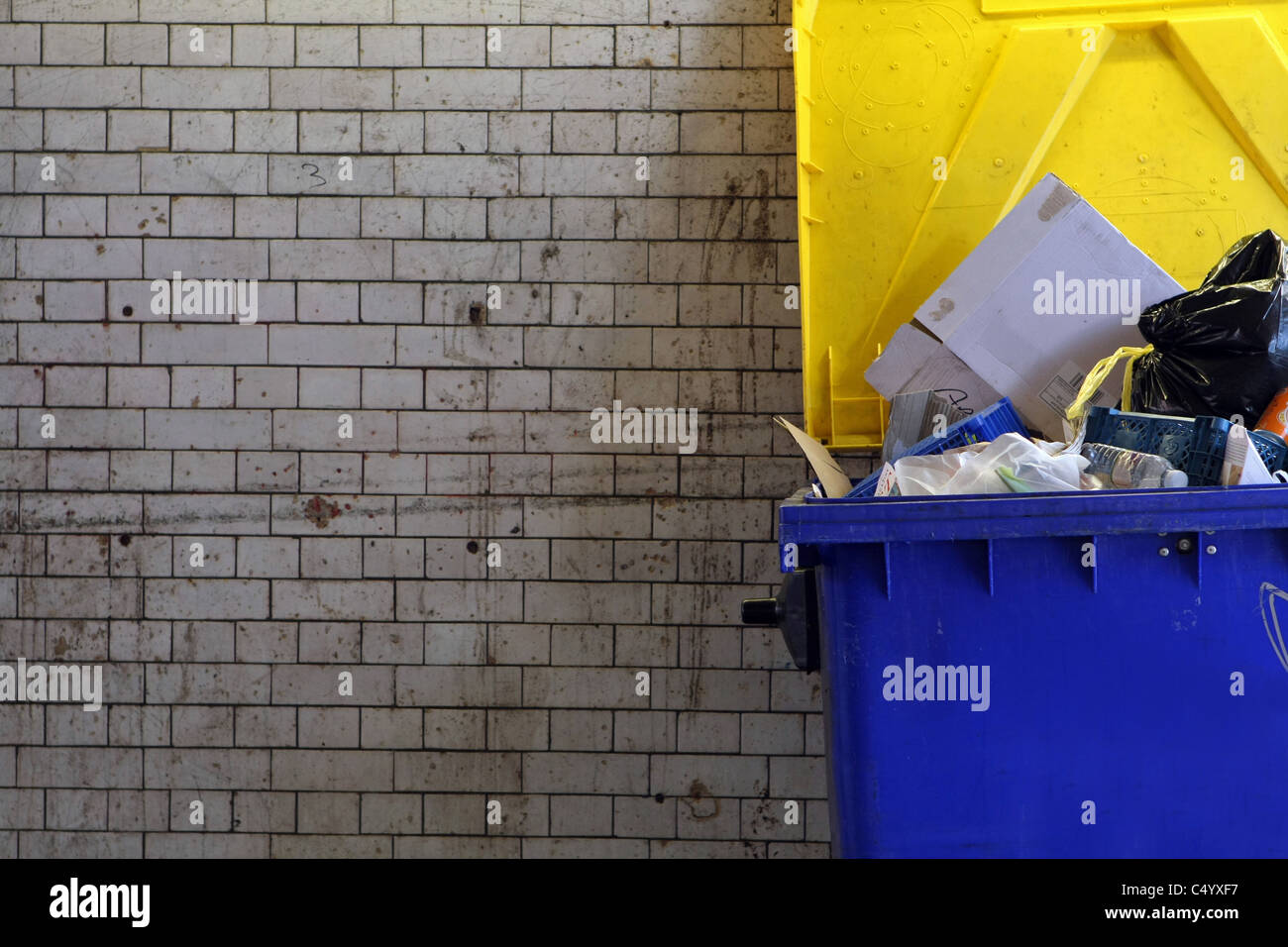 Part of a commercial wheelie bin full of rubbish under a railway arch in London Stock Photo