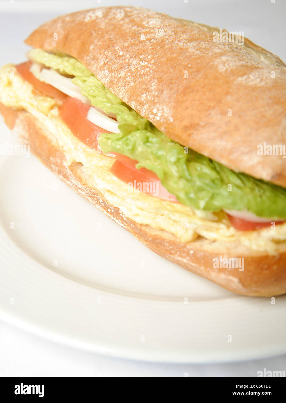 Egg sandwich in a Ciabatta roll with tomato and lettuce on a white plate Stock Photo