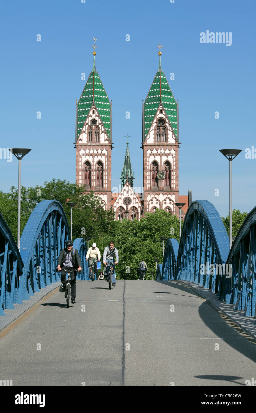 Cyclists crossing the Blue Bruecke (Blue Bridge), a cycle/pedestrian route over railway lines, Freiburg, Germany. The Herz Jesu Church behind. Stock Photo