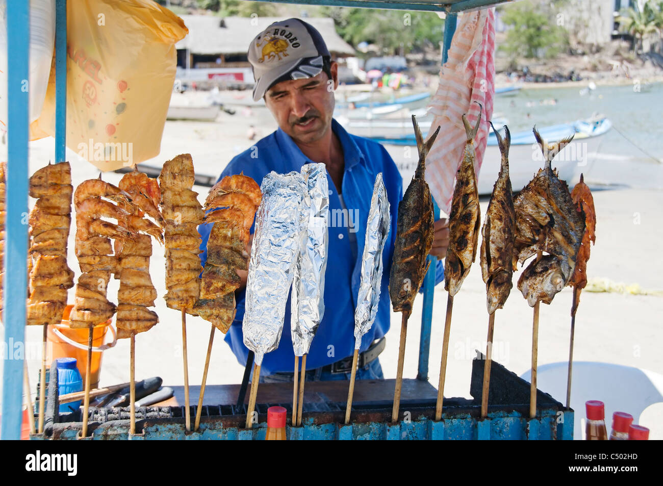 A man sells fresh, delicious barbecued shrimp and fish from a push cart on the beach in Rincon de Guayabitos, Nayarit, Mexico. Stock Photo