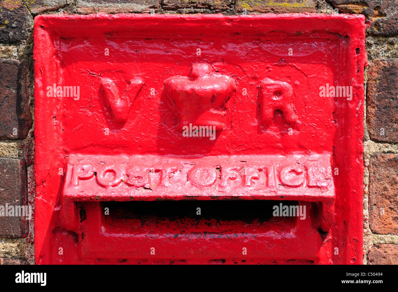 A close-up photo of a red Victorian-made British Royal Mail letter/post box built into a brick wall. Stock Photo