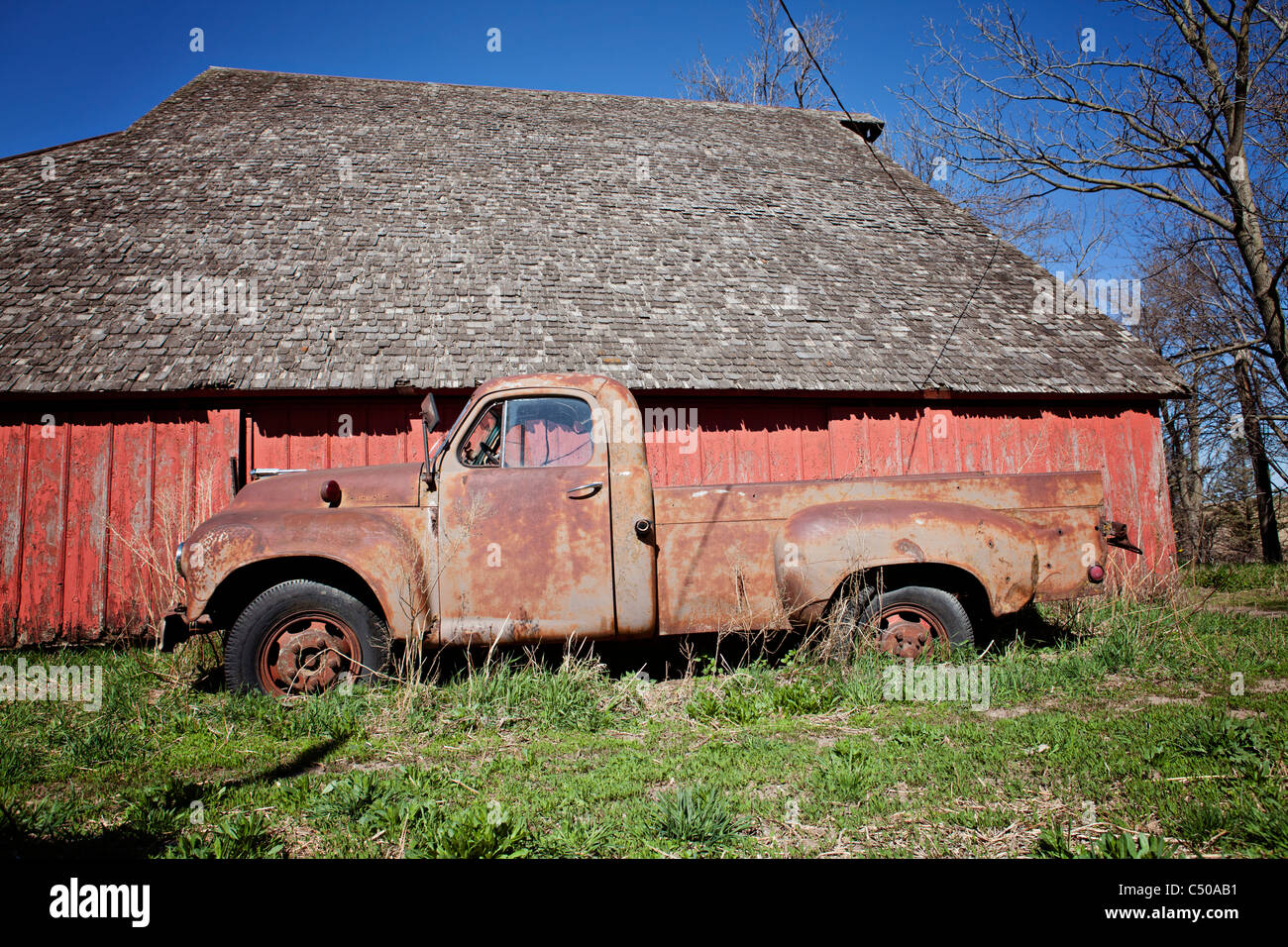 Old rusted truck sitting in front of old red barn in Iowa. Stock Photo
