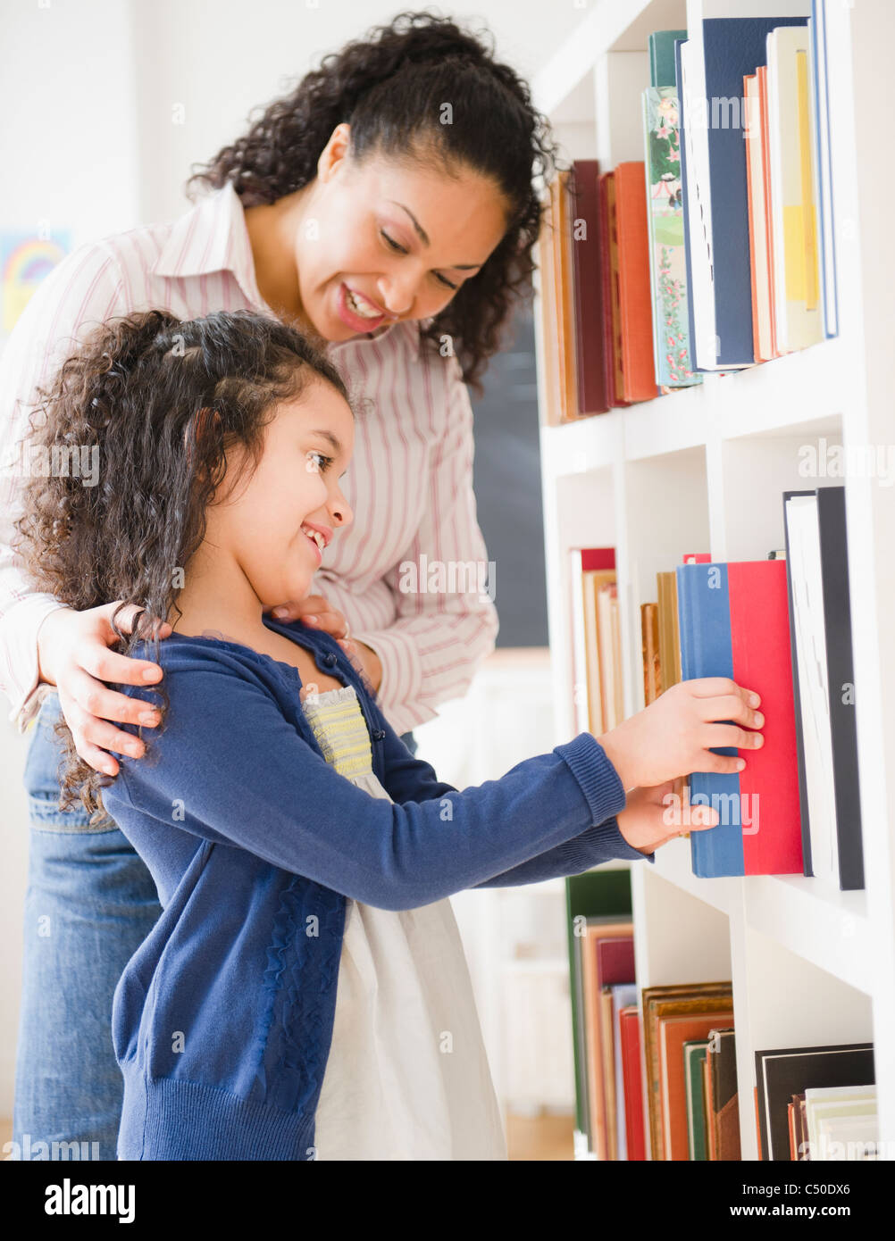 Mother helping daughter choose book on shelf Stock Photo