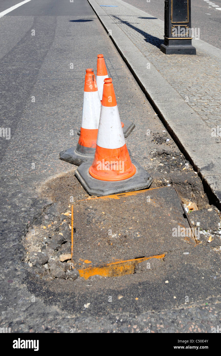 Potholes around manhole cover in London street marked by road traffic cones England UK Stock Photo