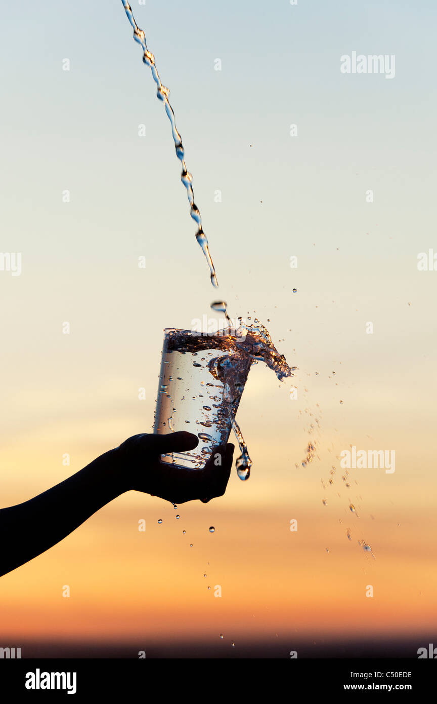 Water being poured into a plastic cup at sunset. Silhouette. India Stock Photo