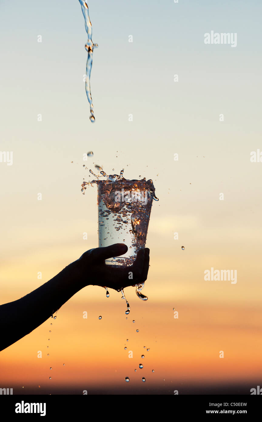 Water being poured into a plastic cup at sunset. Silhouette. India Stock Photo