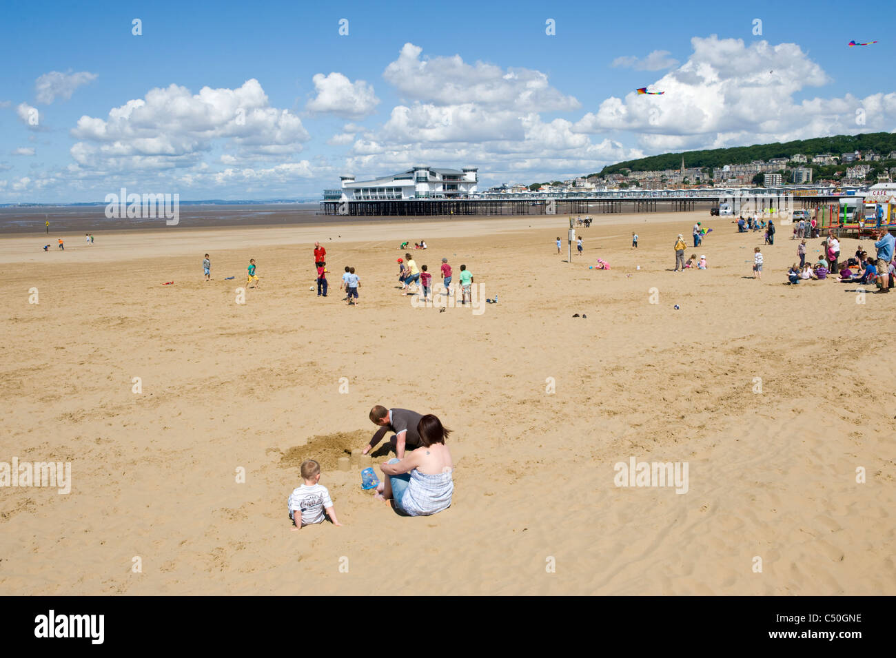 Family groups on the sand beach with pier in background at Weston Super Mare Somerset England UK Stock Photo
