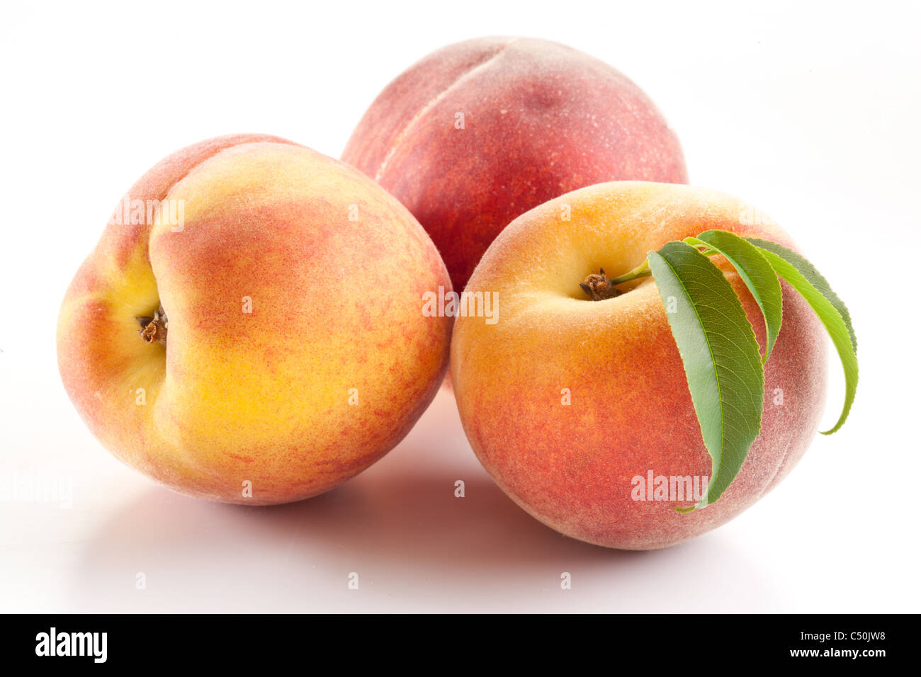Three ripe peach with leaves on white background. Stock Photo