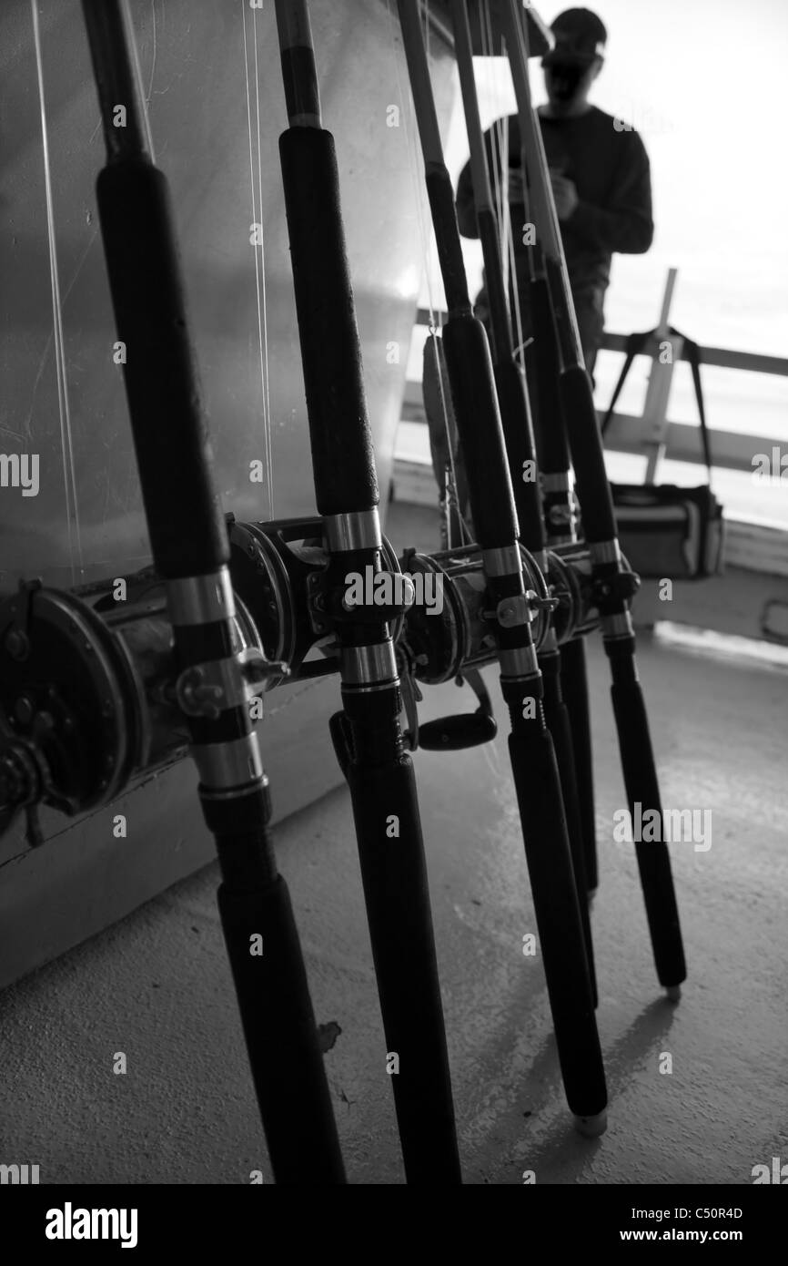 Fishing rods and bait caster reels lined up in a row on a deep sea fishing boat in black and white. Stock Photo