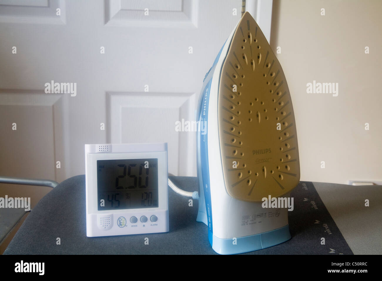 Close up Electricity monitor on an ironing board alongside a switched on iron Stock Photo