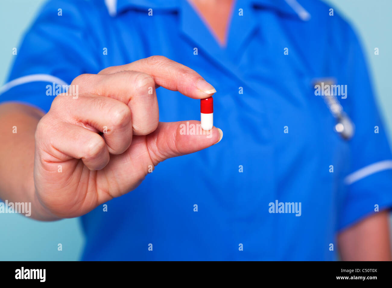 Photo of a nurse in uniform holding a pill towards camera, focus is on the pill. Stock Photo