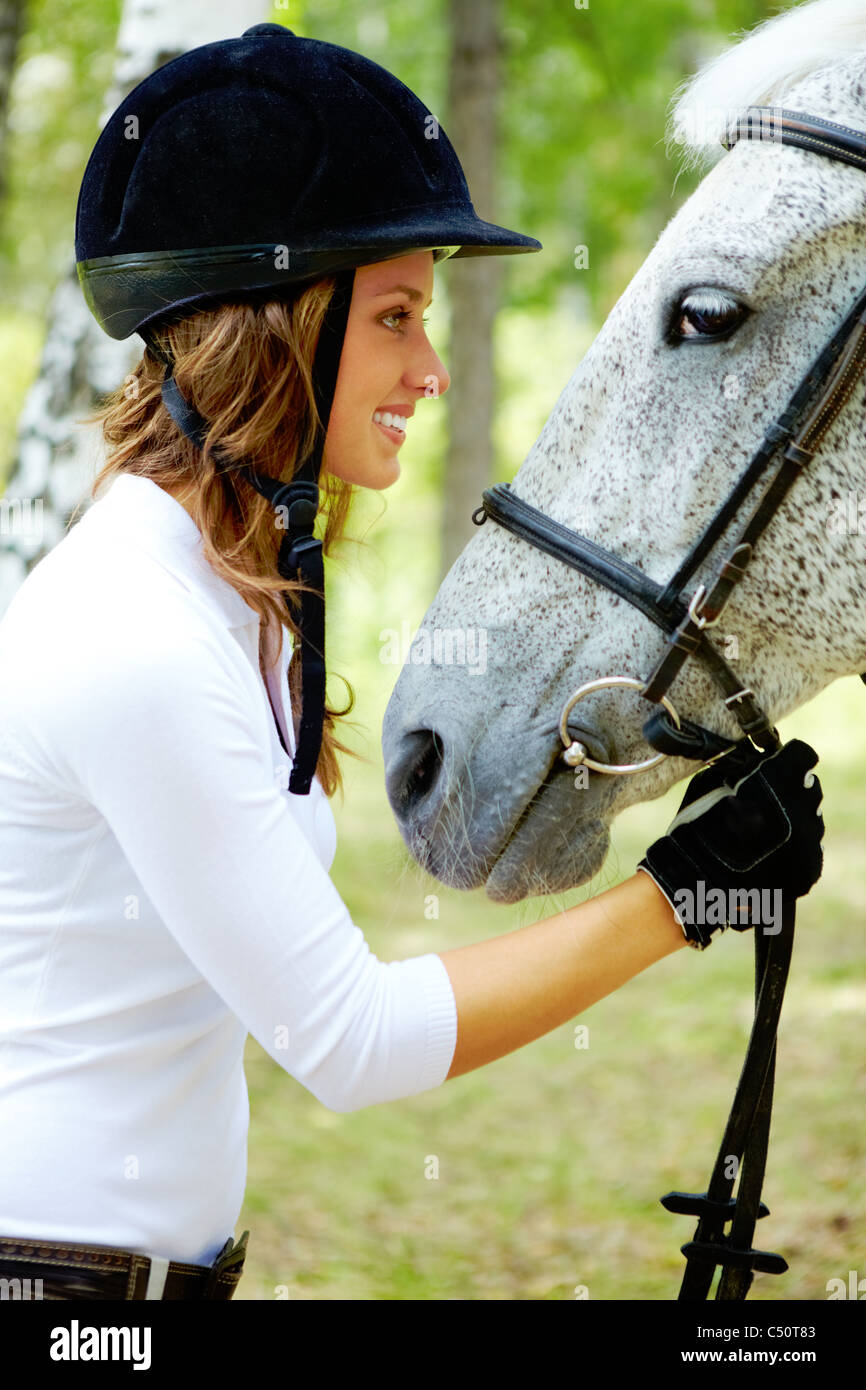 Image of happy female in riding cap holding purebred horse by bridle