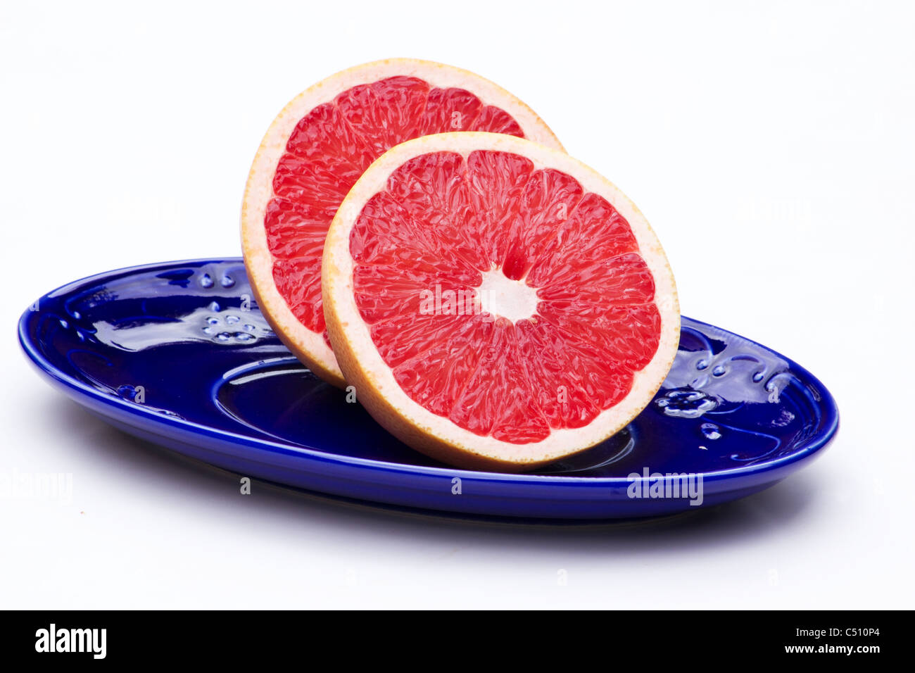 Close-up of grapefruit cut in half in a blue dish on white background Stock Photo
