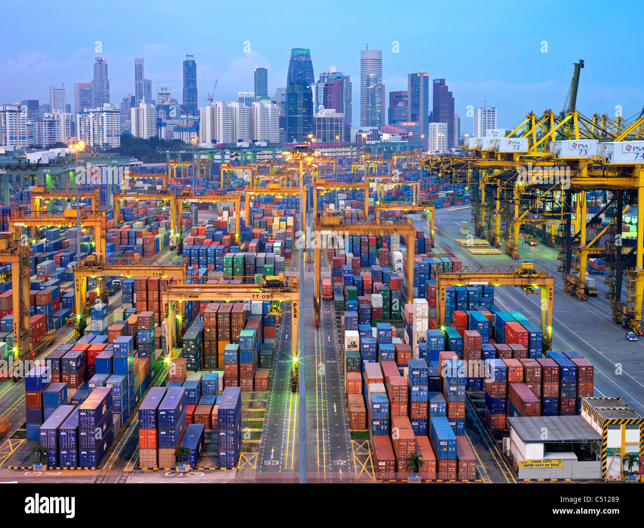 An evening view of a Singapore container terminal just after dusk with the contrast of the city in the background Stock Photo
