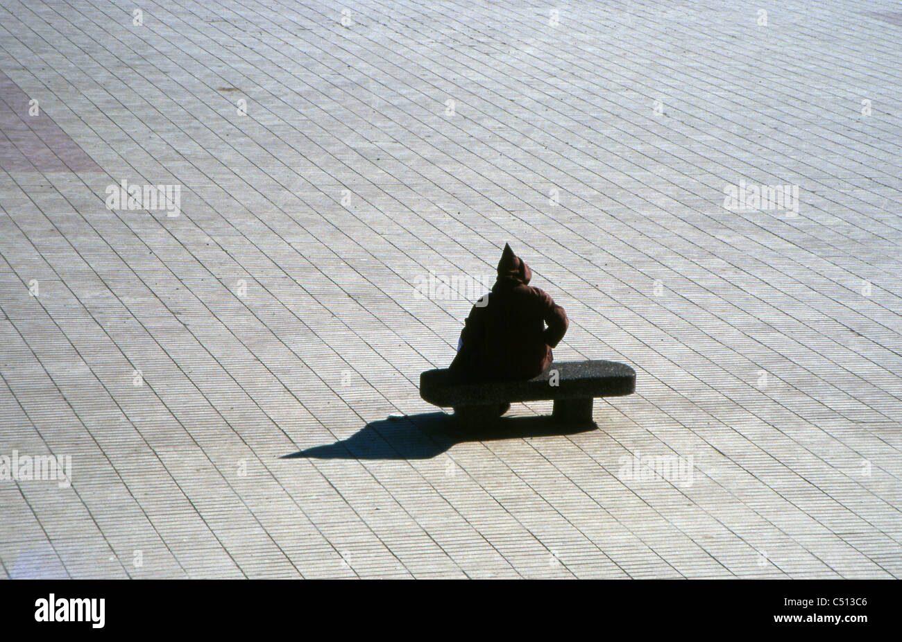 Hooded figure sitting alone on bench Stock Photo
