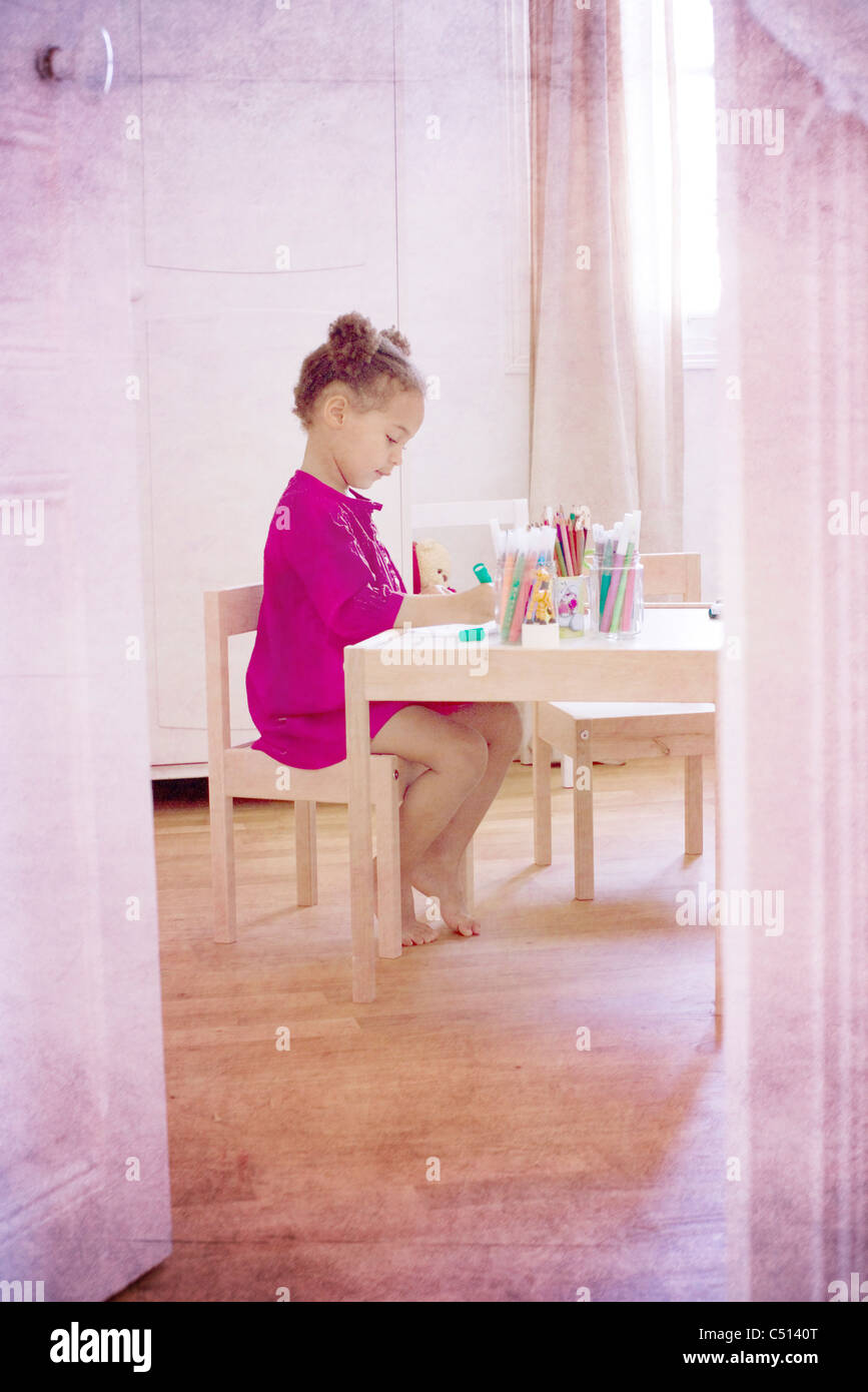Little girl sitting at desk drawing Stock Photo