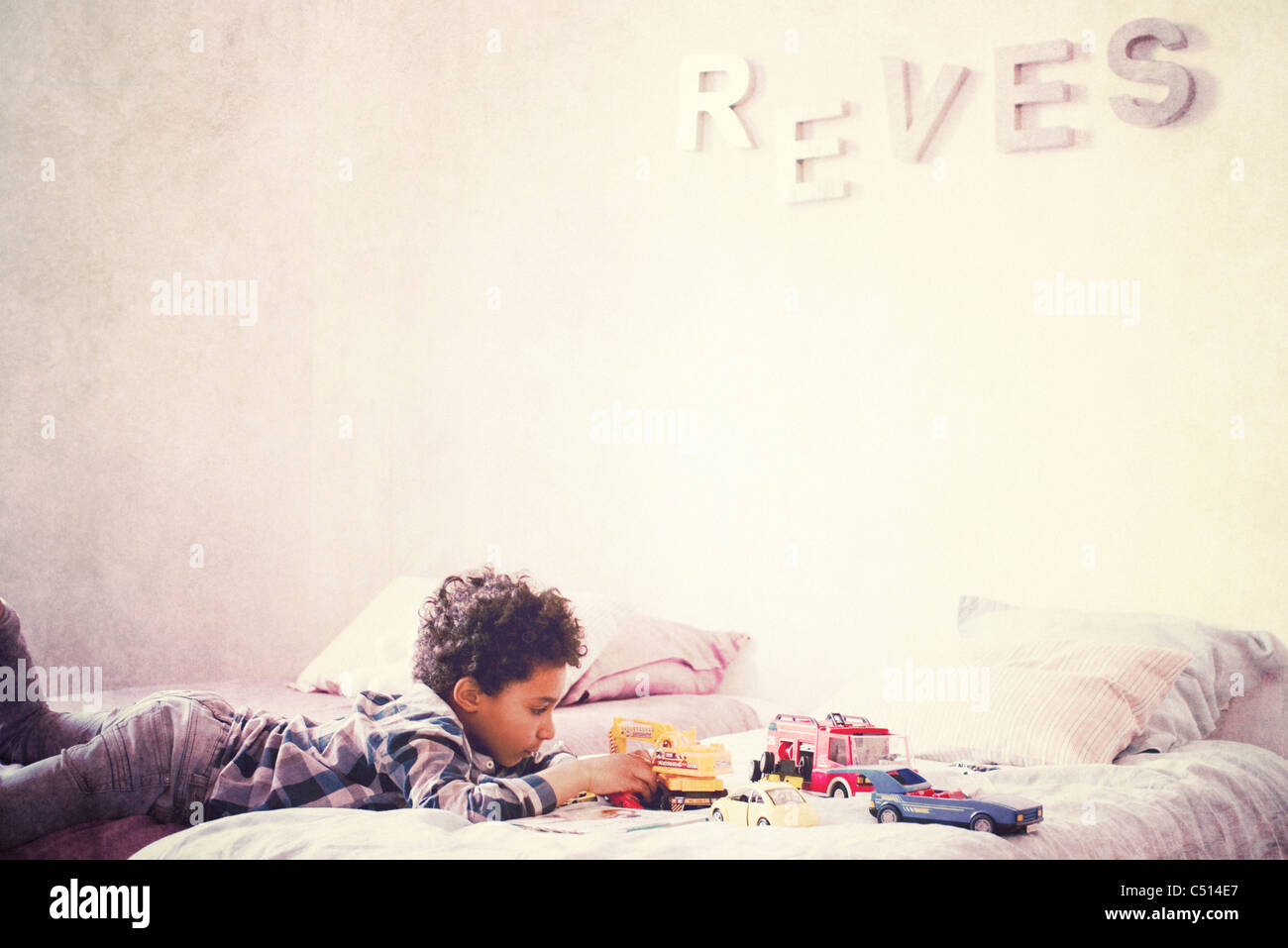 Little boy lying on stomach on bed playing with toy cars Stock Photo