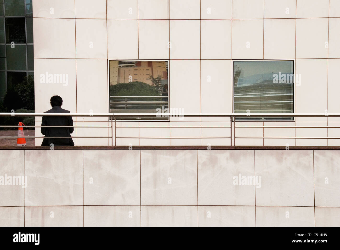 Man leaning against railing outside of building, rear view Stock Photo