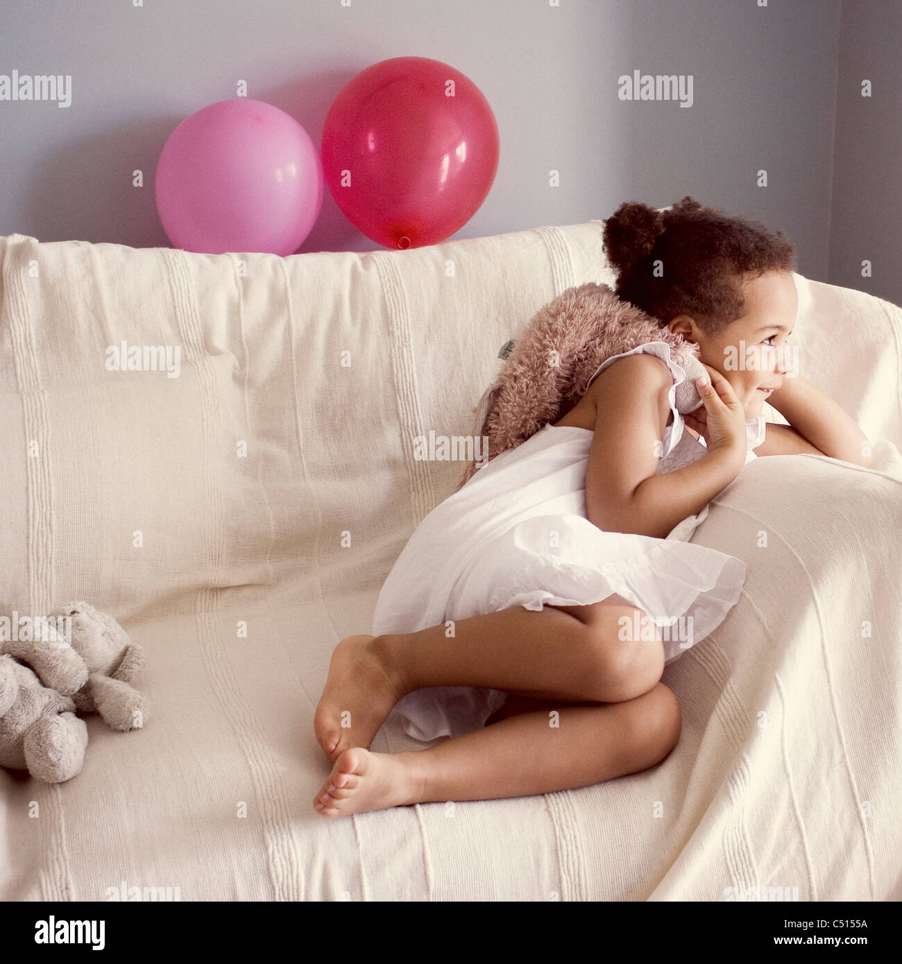 Smiling little girl lying on couch with stuffed toy in hand Stock Photo