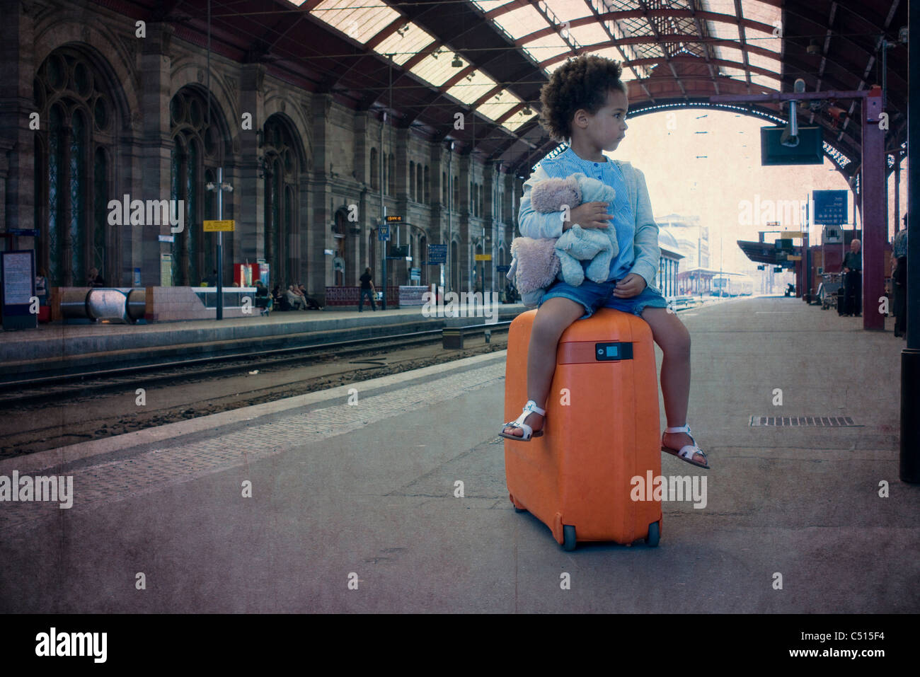 Little girl sitting on suitcase waiting in train station Stock Photo