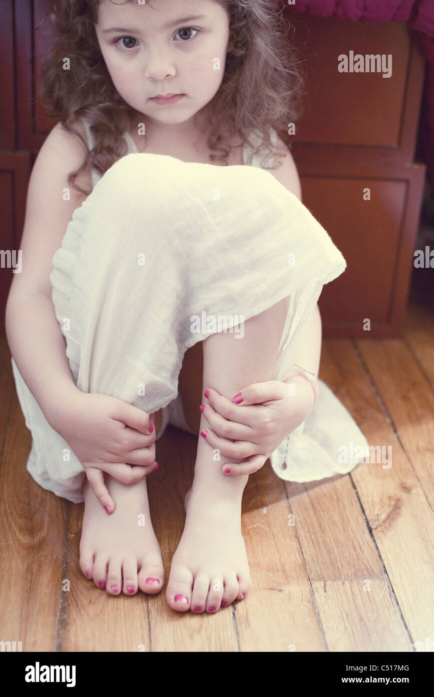 Littles girl in dress hugging knees, portrait Stock Photo