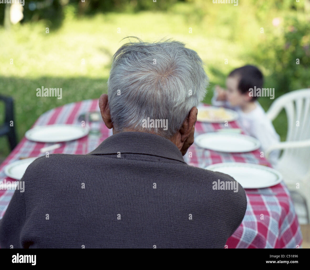 Senior man sitting at table outdoors, contemplating grandchild Stock Photo
