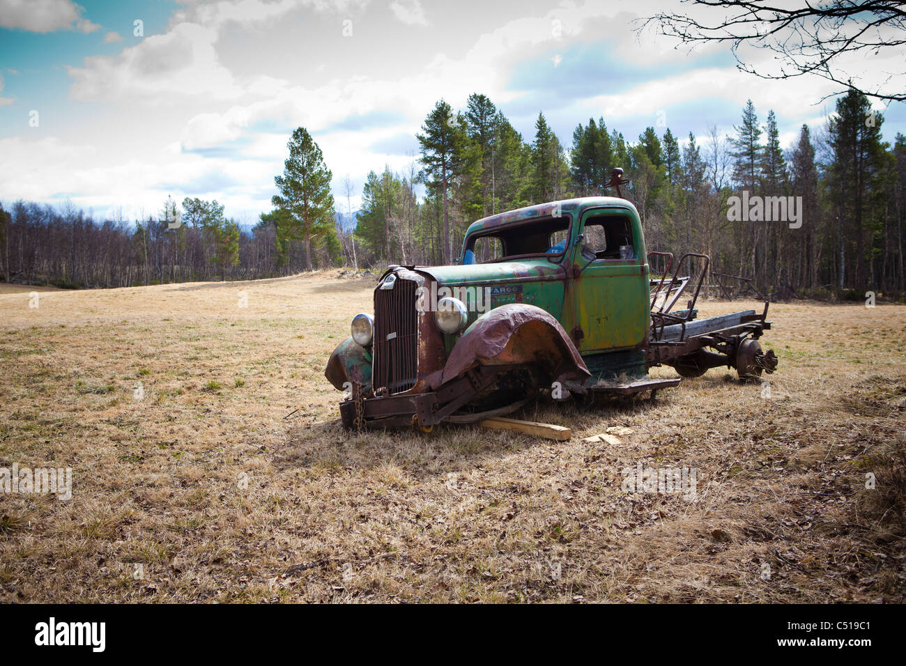 A rusted truck left in a barren field in the wilderness with looming in clouds Stock Photo