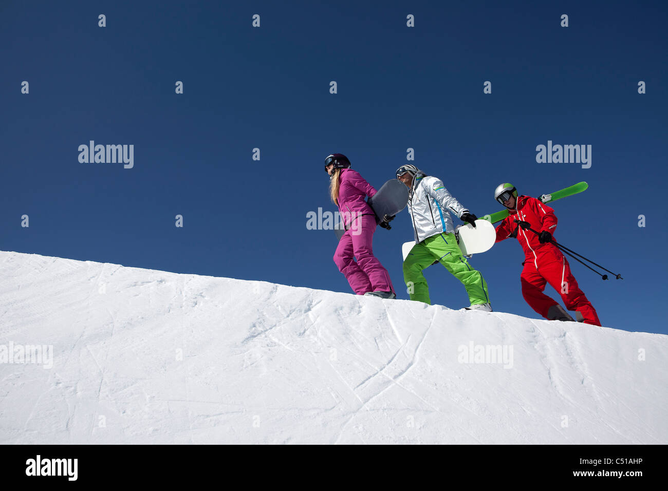 group of three people with skis and snowboards walking up mountain Stock Photo