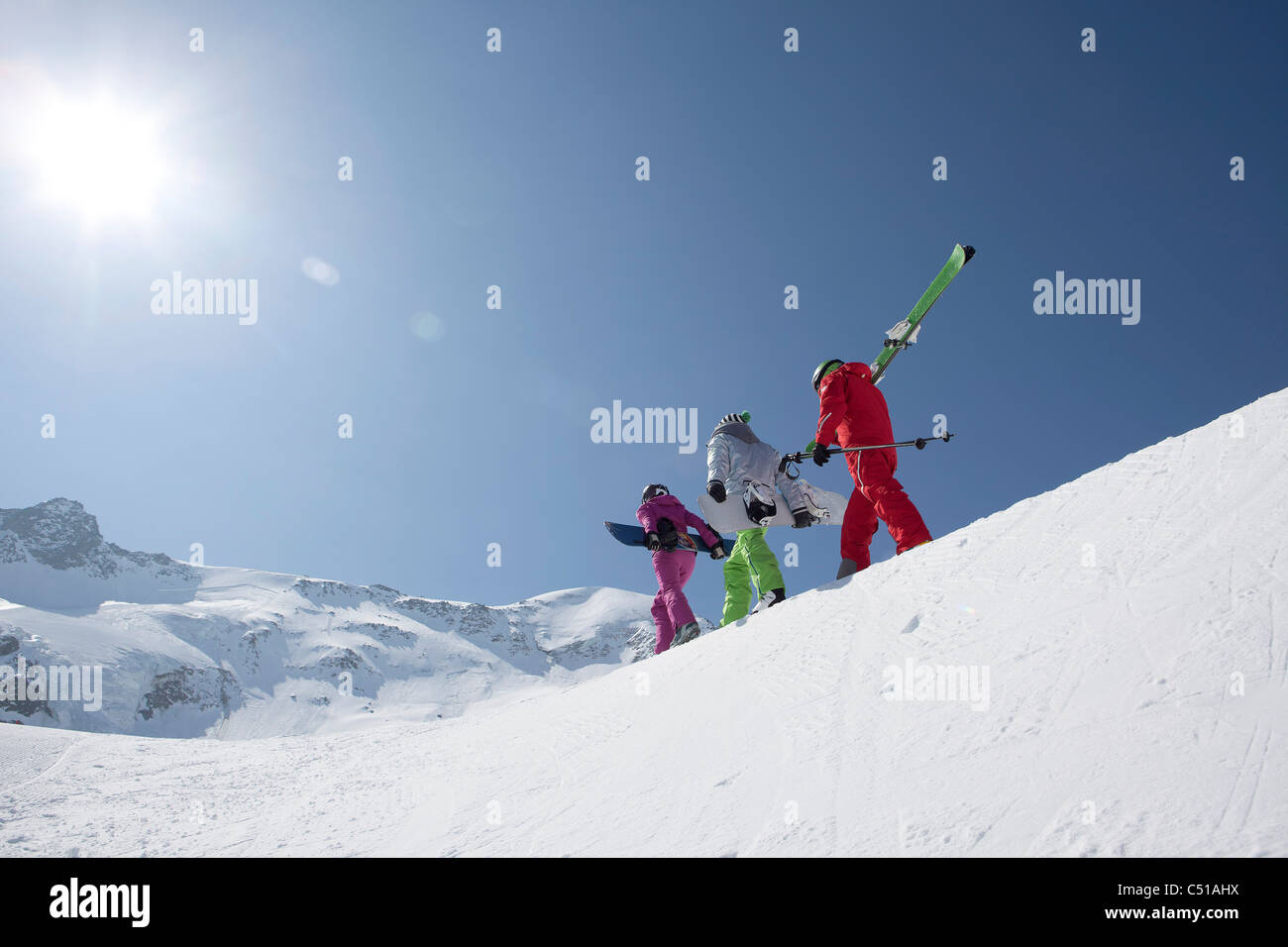 group of three people with skis and snowboards walking up mountain Stock Photo