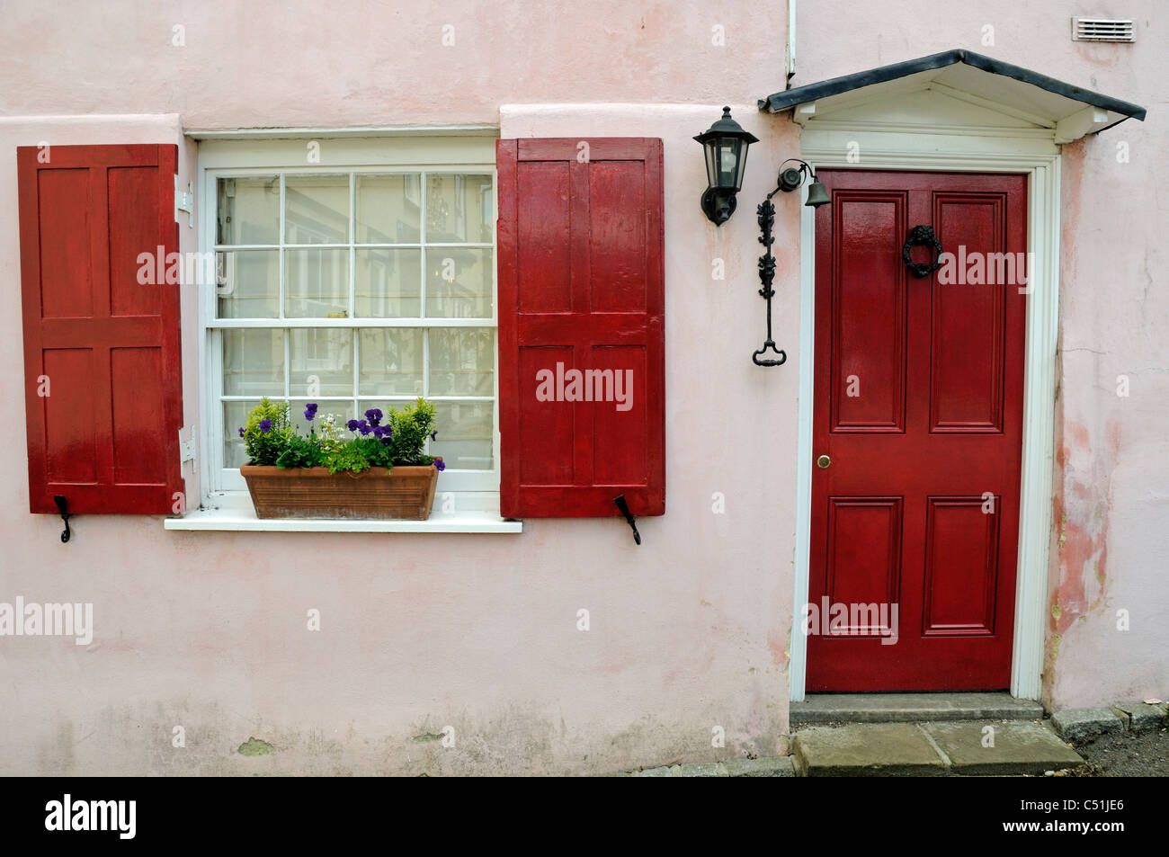 Red wooden window shutters and door on pink painted cottage with black ironwork Braughing Village Hertfordshire England UK Stock Photo